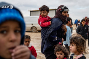 An elderly Syrian woman carries a toddler as others gather at the Washukanni camp, photo by Delil SOULEIMAN, AFP